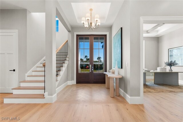 foyer with a raised ceiling, french doors, light hardwood / wood-style floors, and an inviting chandelier