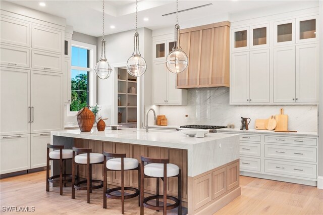 kitchen featuring backsplash, white cabinets, sink, decorative light fixtures, and a large island