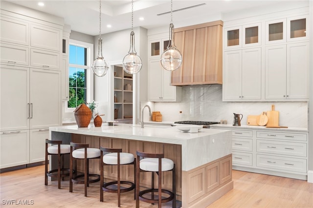 kitchen with pendant lighting, a spacious island, glass insert cabinets, white cabinets, and light wood-type flooring