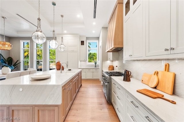 kitchen with a tray ceiling, a spacious island, decorative light fixtures, white cabinets, and stainless steel stove