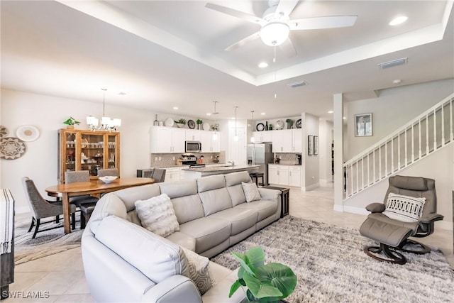 tiled living room featuring ceiling fan with notable chandelier and a raised ceiling