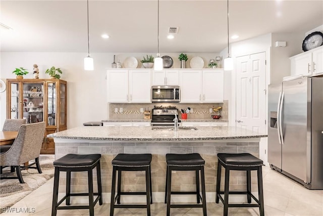 kitchen with stainless steel appliances, decorative light fixtures, white cabinetry, a breakfast bar area, and an island with sink