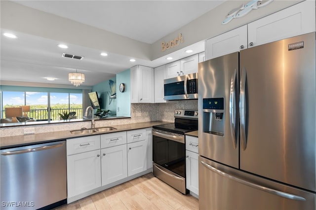 kitchen with sink, light wood-type flooring, white cabinetry, stainless steel appliances, and a chandelier