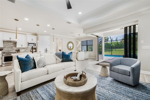 living room featuring light hardwood / wood-style floors, ceiling fan, ornamental molding, and a tray ceiling