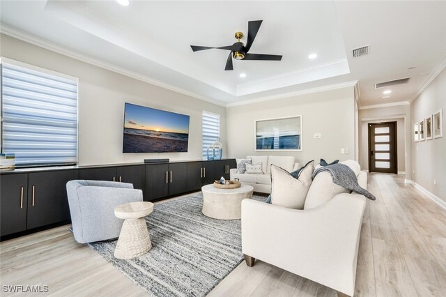 living room with a tray ceiling, crown molding, ceiling fan, and light wood-type flooring