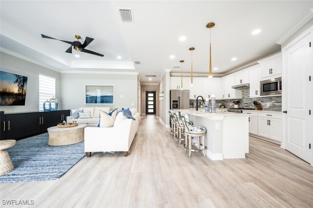 kitchen with stainless steel appliances, a tray ceiling, a kitchen island with sink, pendant lighting, and white cabinets