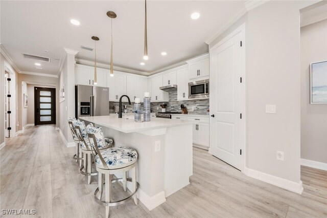 kitchen with backsplash, stainless steel appliances, pendant lighting, a center island with sink, and white cabinets