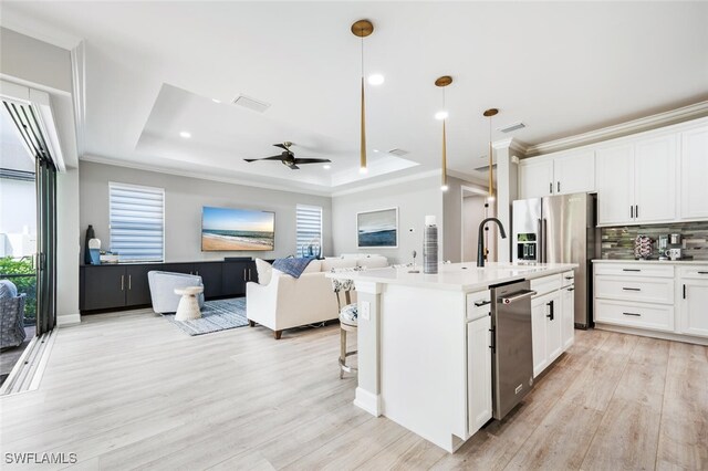 kitchen with decorative light fixtures, a raised ceiling, white cabinetry, and a kitchen island with sink