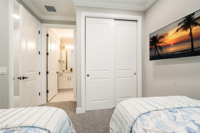 bedroom with crown molding, a closet, light colored carpet, visible vents, and ensuite bathroom