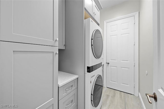 laundry room featuring cabinets, stacked washing maching and dryer, and light hardwood / wood-style flooring