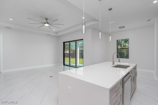 kitchen with a raised ceiling, ceiling fan, sink, pendant lighting, and an island with sink