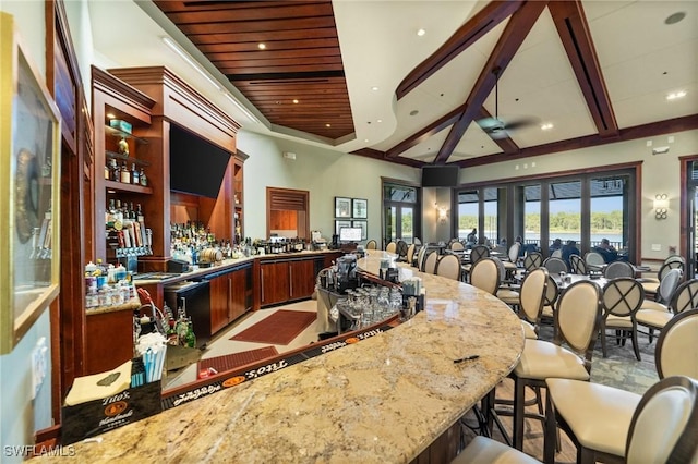 kitchen with kitchen peninsula, light stone countertops, beamed ceiling, and ceiling fan