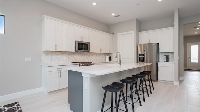 kitchen featuring a breakfast bar, light countertops, appliances with stainless steel finishes, white cabinets, and a kitchen island with sink