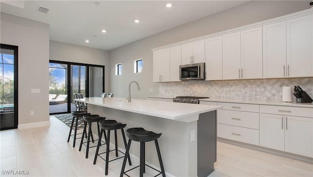 kitchen featuring tasteful backsplash, stainless steel microwave, visible vents, a sink, and range