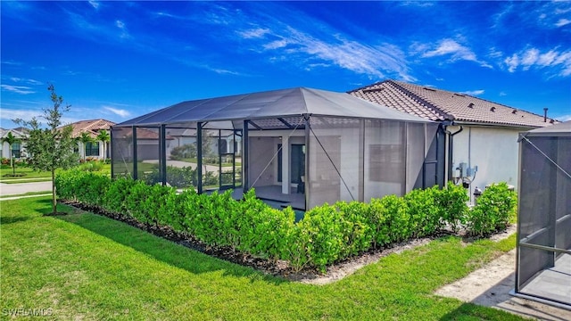 rear view of property featuring a lanai, a tiled roof, a yard, and stucco siding