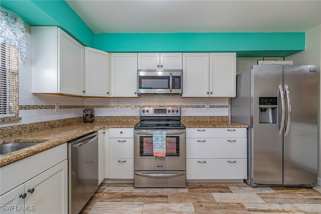 kitchen featuring appliances with stainless steel finishes, light wood-type flooring, backsplash, stone countertops, and white cabinetry