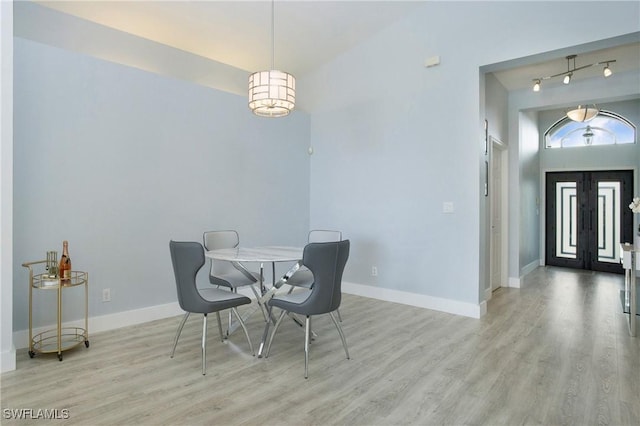 dining room with light wood-style floors, french doors, rail lighting, and baseboards