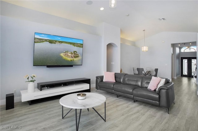 living area with arched walkways, lofted ceiling, visible vents, light wood-style floors, and baseboards