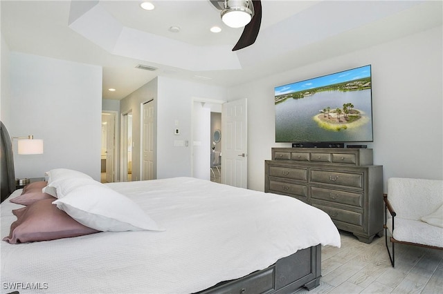 bedroom featuring visible vents, a ceiling fan, a tray ceiling, light wood-style floors, and recessed lighting