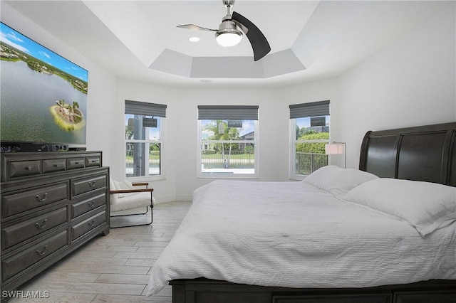 bedroom featuring light wood-type flooring, ceiling fan, a tray ceiling, and baseboards