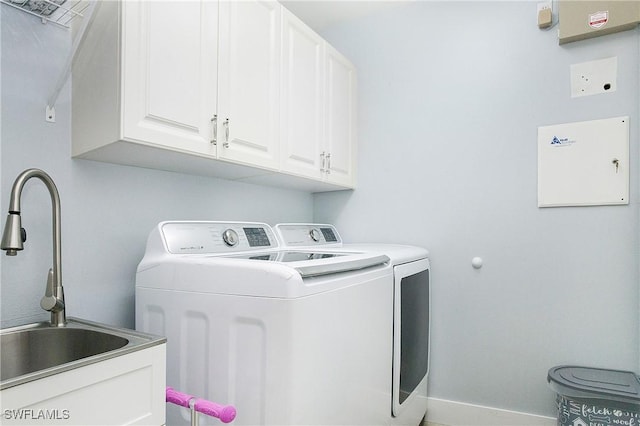 clothes washing area with cabinet space, washing machine and dryer, baseboards, and a sink