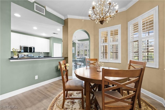 dining room with light hardwood / wood-style floors, plenty of natural light, ornamental molding, and a notable chandelier