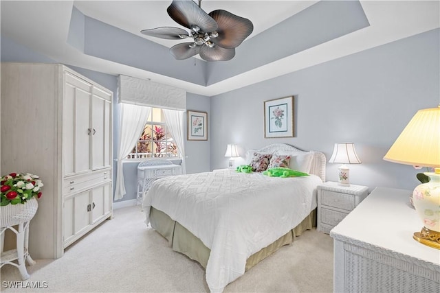 carpeted bedroom with ceiling fan and a tray ceiling