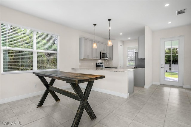 kitchen with sink, gray cabinets, light stone countertops, decorative light fixtures, and kitchen peninsula