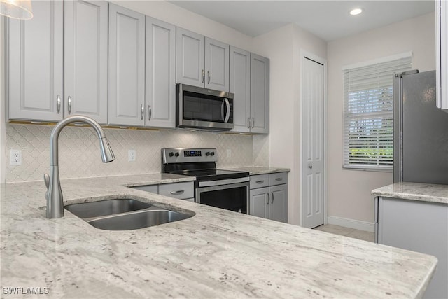 kitchen with light stone countertops, tasteful backsplash, gray cabinetry, stainless steel appliances, and sink