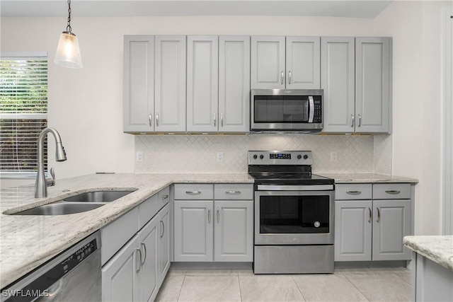 kitchen featuring light stone countertops, appliances with stainless steel finishes, sink, pendant lighting, and gray cabinets