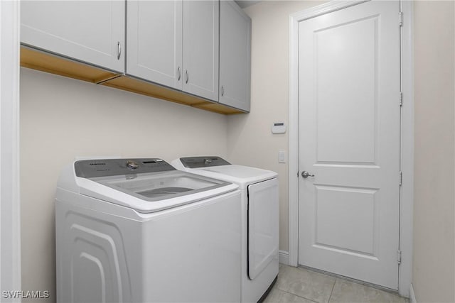 laundry area with washing machine and dryer, light tile patterned floors, and cabinets