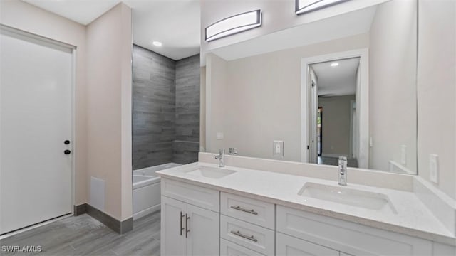 bathroom with double vanity, a bathtub, a sink, and wood finished floors