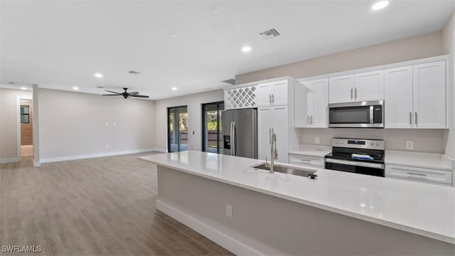 kitchen featuring white cabinets, light wood-style flooring, stainless steel appliances, light countertops, and a sink