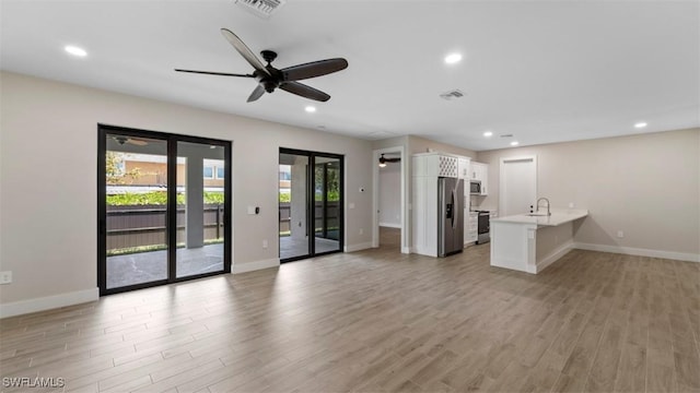 unfurnished living room with ceiling fan, sink, and light wood-type flooring