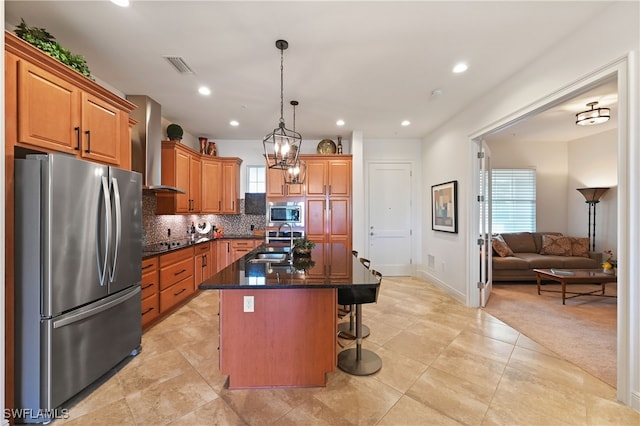 kitchen with sink, wall chimney exhaust hood, stainless steel appliances, pendant lighting, and a center island with sink