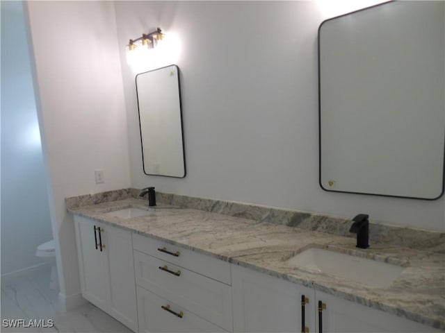 bathroom with toilet, marble finish floor, double vanity, and a sink