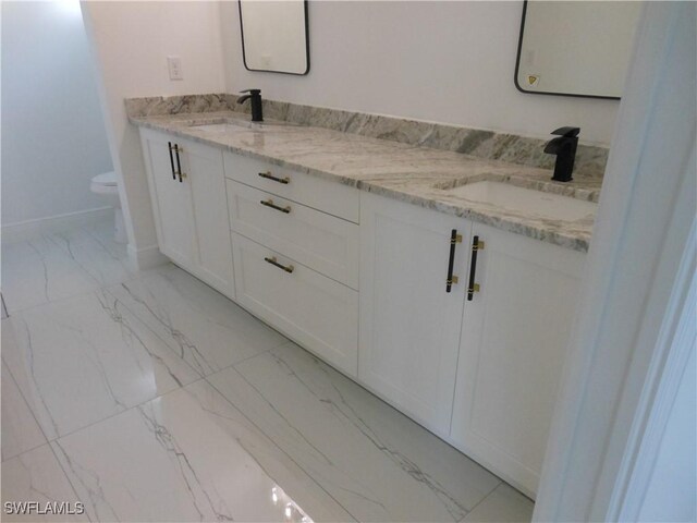 bathroom with marble finish floor, double vanity, a sink, and toilet