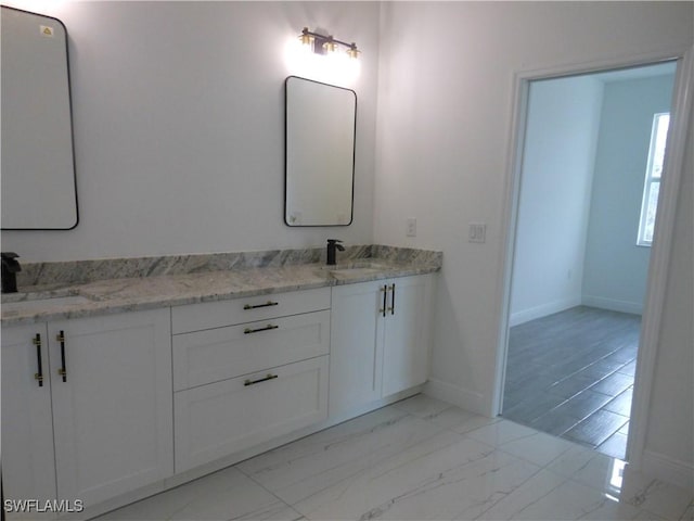 full bath featuring marble finish floor, a sink, baseboards, and double vanity