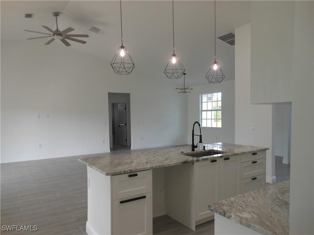 kitchen with pendant lighting, white cabinetry, an island with sink, sink, and light stone counters