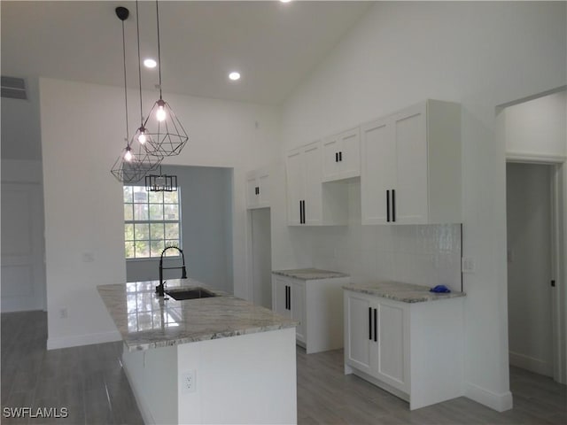 kitchen with sink, hanging light fixtures, a center island with sink, light stone countertops, and white cabinets