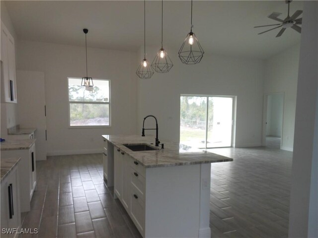 kitchen featuring white cabinetry, decorative light fixtures, a kitchen island with sink, and sink