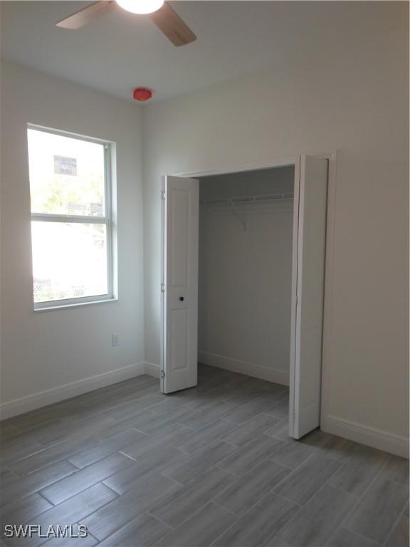 unfurnished bedroom featuring light wood-type flooring, ceiling fan, baseboards, and a closet