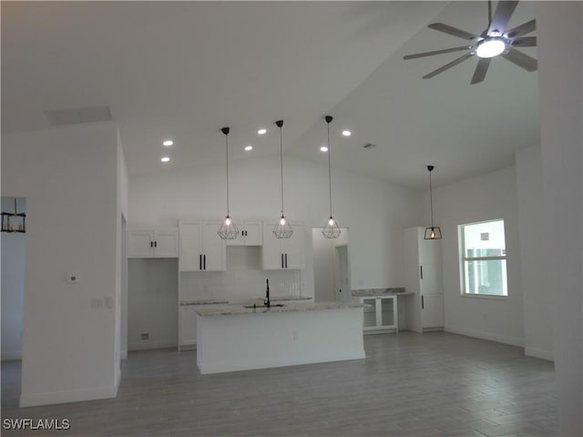 kitchen with sink, light stone counters, white cabinetry, high vaulted ceiling, and a kitchen island with sink