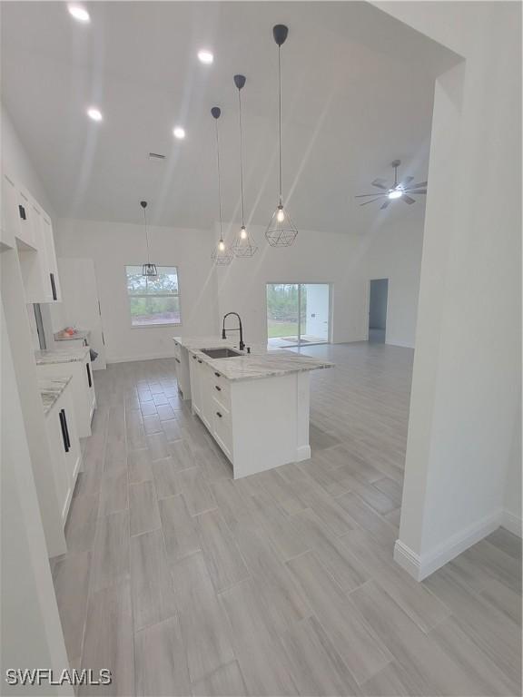 kitchen with a center island with sink, white cabinets, open floor plan, pendant lighting, and a sink