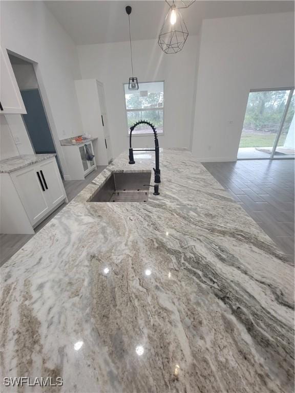 kitchen featuring white cabinetry, decorative light fixtures, light stone countertops, and sink