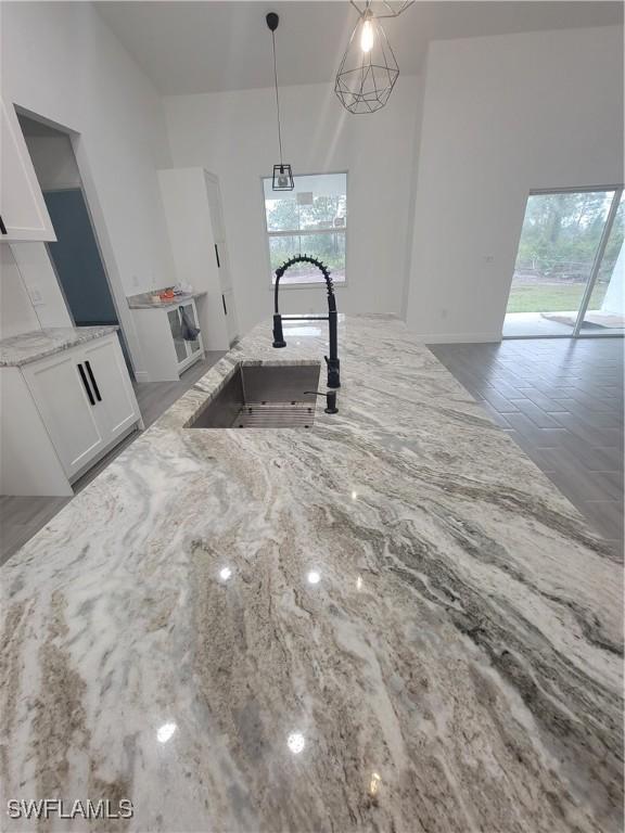 kitchen with hanging light fixtures, white cabinetry, light stone counters, and a sink