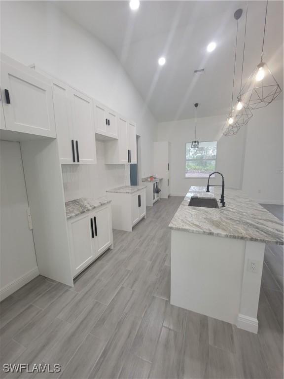 kitchen featuring a kitchen island with sink, white cabinets, and decorative light fixtures