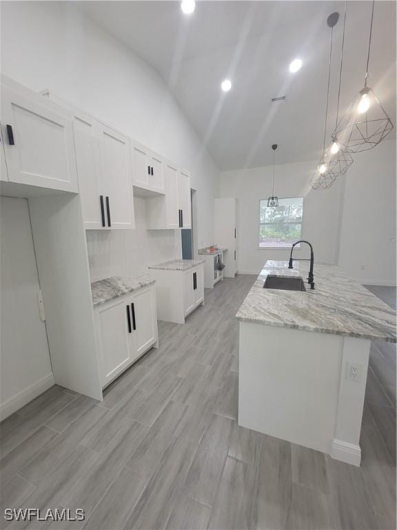 kitchen with white cabinets, decorative light fixtures, and an island with sink