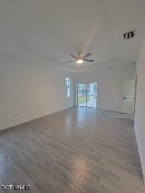 empty room with ceiling fan and a tray ceiling