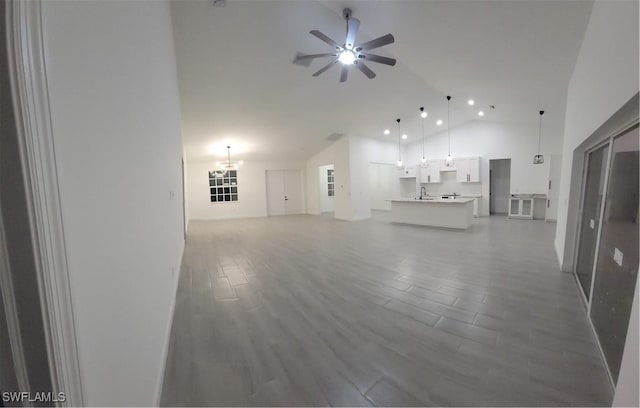 unfurnished living room featuring wood-type flooring, ceiling fan with notable chandelier, and high vaulted ceiling